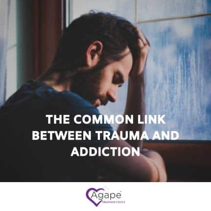 Person sitting by window, holding head in hands, with text The Common Link Between Trauma and Addiction.