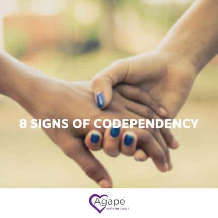 Two hands holding with blue nail polish and 8 Signs of Codependency text.