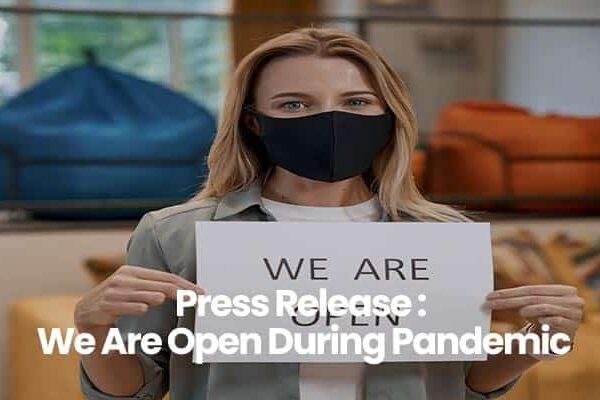 Person holding We Are Open sign wearing a black mask, standing in store.