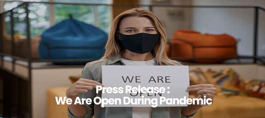 Person holding We Are Open sign wearing a black mask, standing in store.