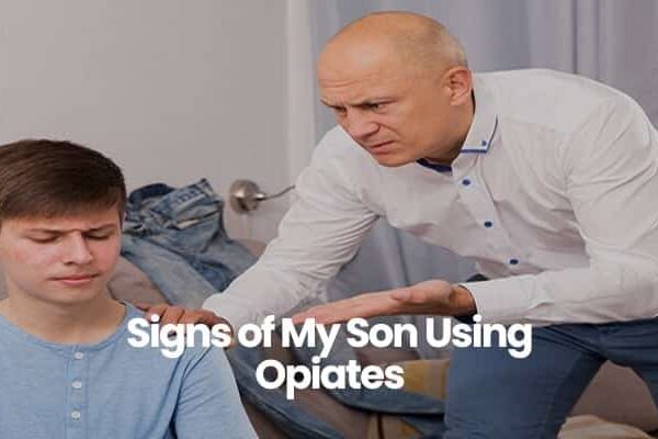 Older man in white shirt talking to younger man in blue shirt on couch.