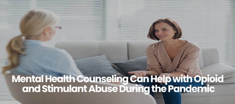 Two women sitting on a couch, one in beige shirt talking to another in blue shirt.