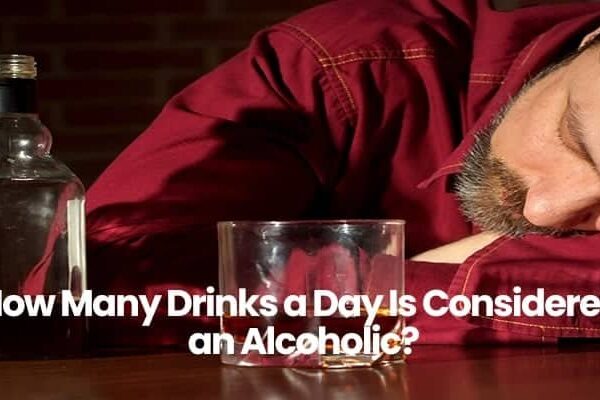 Person in red shirt asleep next to empty glass and bottle on table.