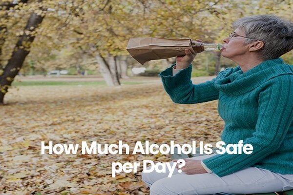 Person in teal sweater drinking from a paper bag in a park with fall leaves.