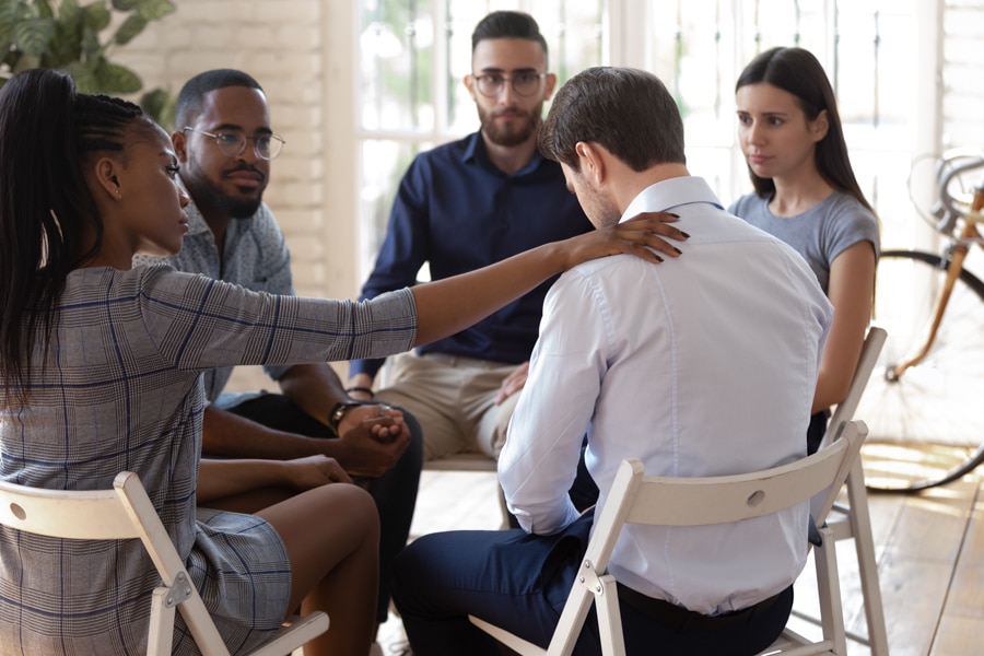 compassionate woman placing a hand on a man's shoulder to support him in group meeting