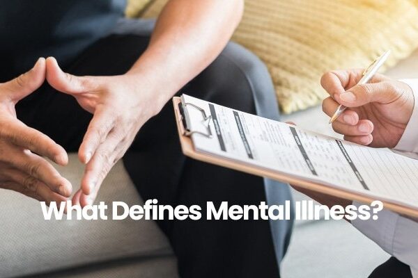 Person with folded hands talking to clipboard holder in white shirt, text What Defines Mental Illness? visible.