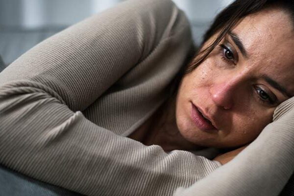 Person resting on sofa, wearing a beige sweater, looking thoughtful.