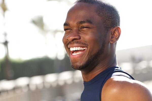 Person wearing a sleeveless shirt and smiling outdoors.