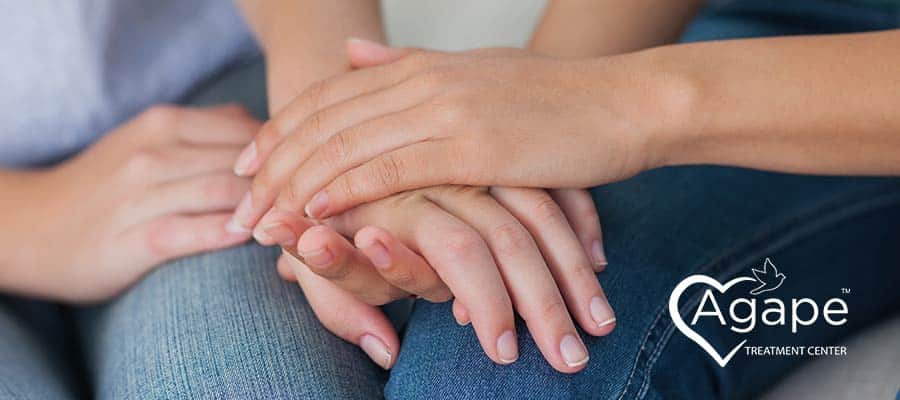 Hands offering comfort with Agape Treatment Center logo in white text and heart design.