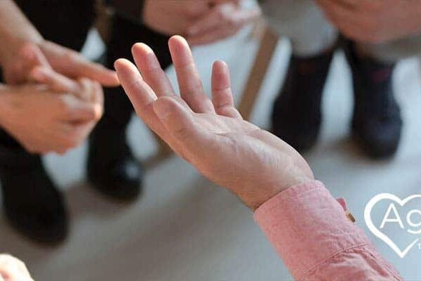 Person in a pink shirt gesturing with hands, surrounded by others sitting, Agape Treatment Center logo nearby.