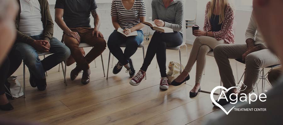 People sitting in a circle with Agape Treatment Center logo in the corner.