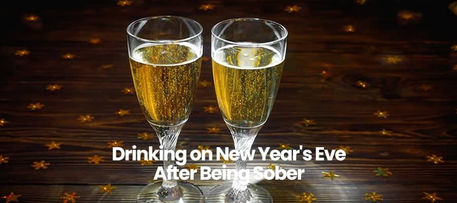 Two champagne glasses on wooden table with New Year's Eve text.