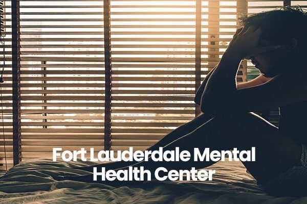 Person sitting on bed, holding head, with blinds in background. Text: Fort Lauderdale Mental Health Center.