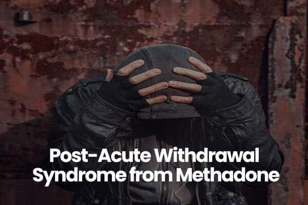Person in black jacket and gloves holding head against rusty metal background.