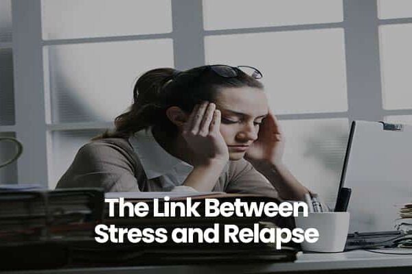 Person sitting at desk, hands on head, with books and a laptop. Text: The Link Between Stress and Relapse.