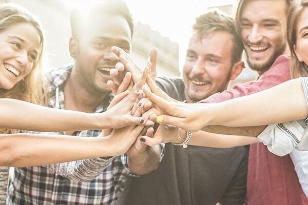 Group of people smiling and touching hands in a gesture of unity.