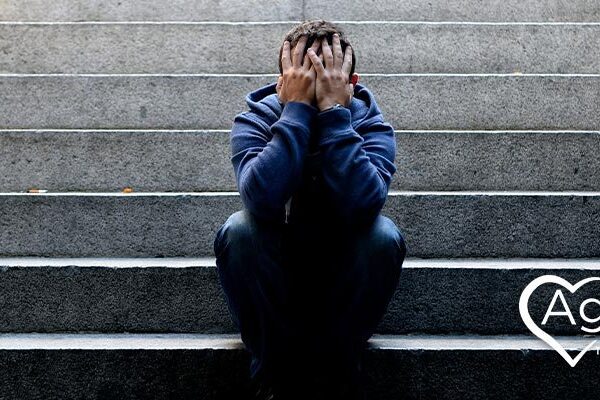 Person in blue hoodie sitting on steps, covering face with hands.