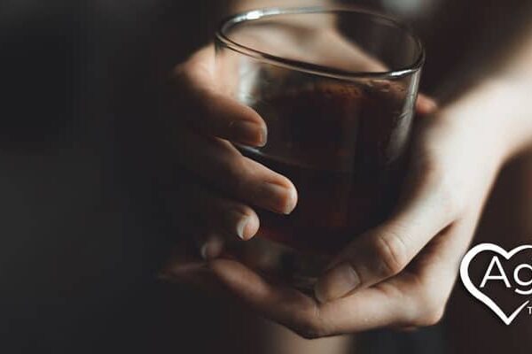 Person holding glass with beverage, logo of Agape Treatment Center in white with heart shape.