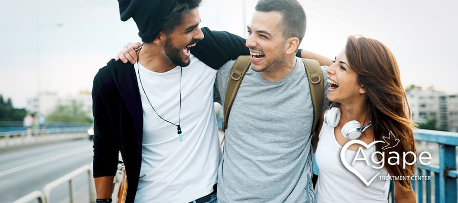 People smiling and embracing on a bridge, with Agape Treatment Center logo.