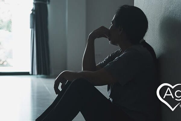 Person sitting on the floor in shadow, with Agape Treatment Center logo on side.