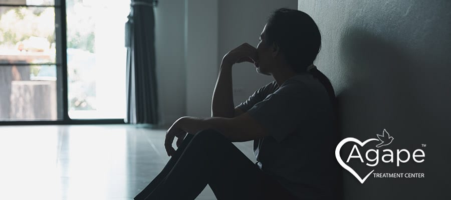 Person sitting on the floor in shadow, with Agape Treatment Center logo on side.
