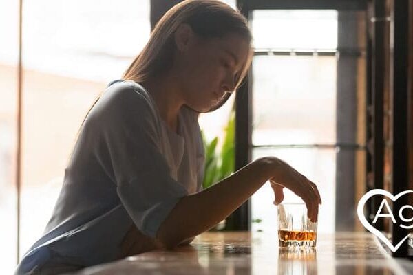 Person sitting at table holding drink with Agape Treatment Center logo in corner.