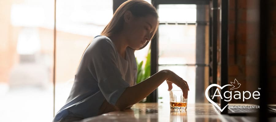 woman sitting alone at a bar with a glass of dark liquor