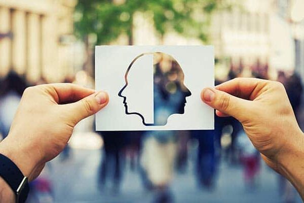 Silhouette of two heads on paper held by hands in a blurred city street.