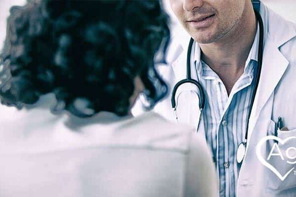 Person wearing a white coat with stethoscope talking to another person.