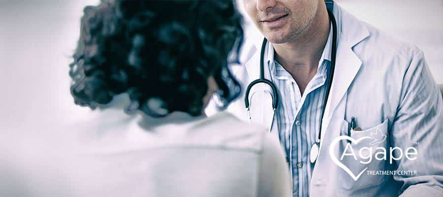 Person wearing a white coat with stethoscope talking to another person.