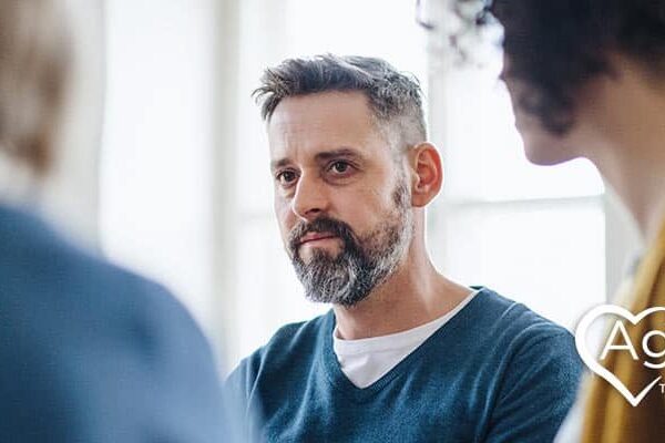 Person with a beard wearing a blue sweater in a discussion group.