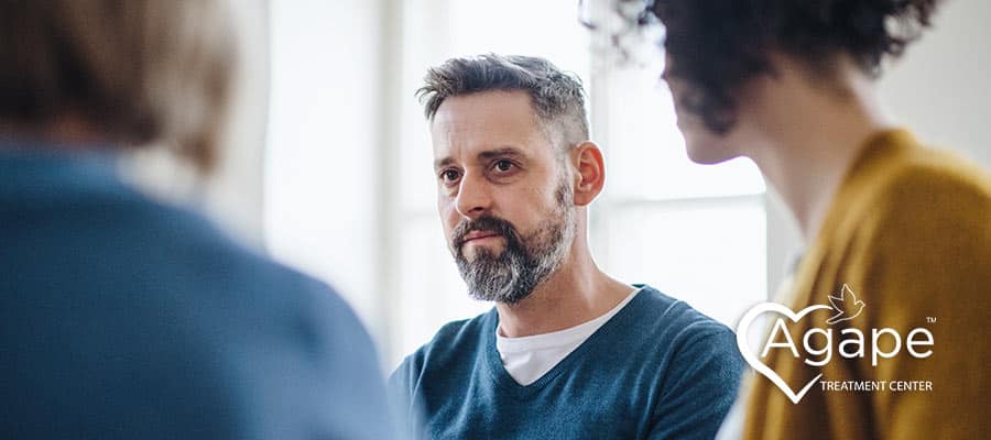 Person with a beard wearing a blue sweater in a discussion group.