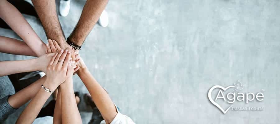 Group of people stacking hands, Agape Treatment Center logo with heart.