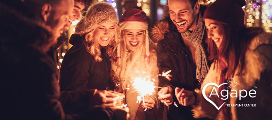 Group of people holding sparklers, wearing winter clothing, smiling under festive lights.