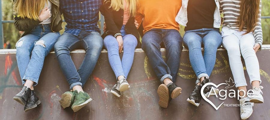 People sitting on a wall wearing casual clothes, logo with heart and Agape Treatment Center.