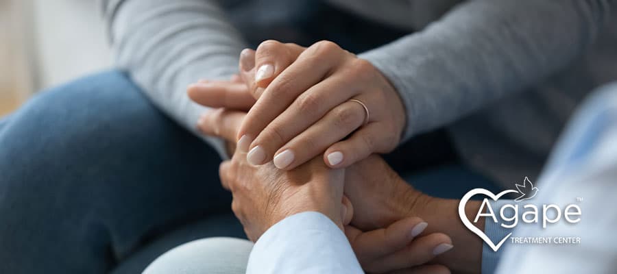 Hands offering comfort with Agape Treatment Center logo in white heart shape.