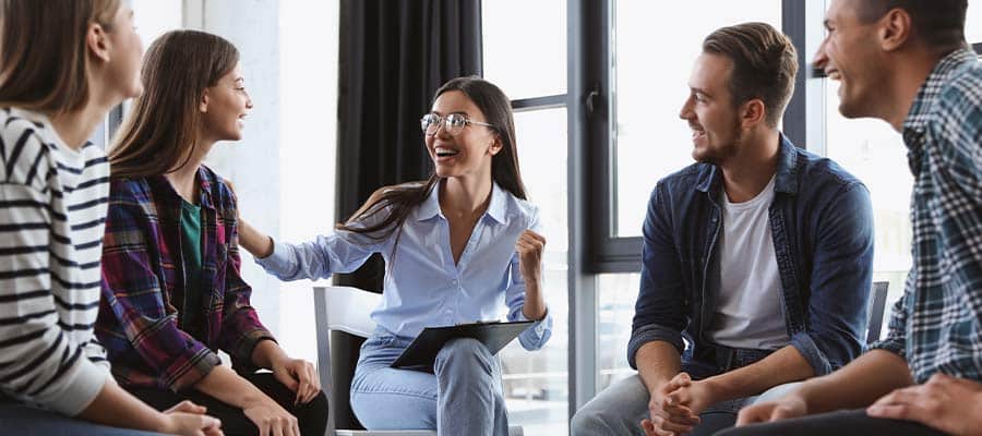Person in light blue shirt with glasses smiling in group discussion.