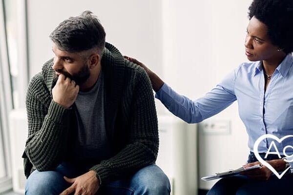Person in blue shirt comforting another in a sweater, Agape Treatment Center logo visible.