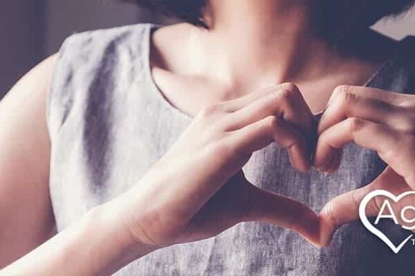 Person in gray sleeveless dress forming a heart shape with hands.
