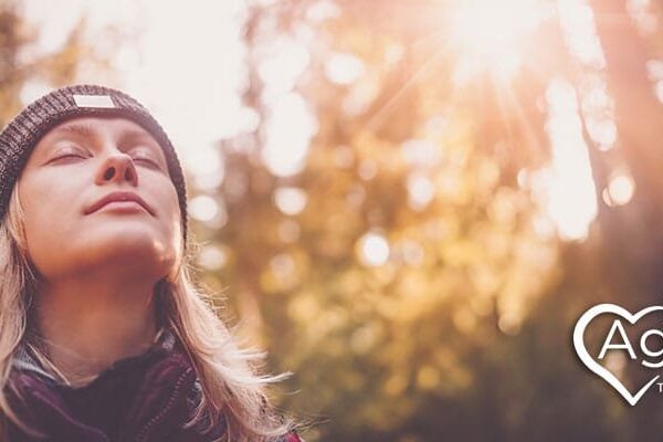Person wearing a beanie and closed eyes in sunlight with Agape Treatment Center logo.