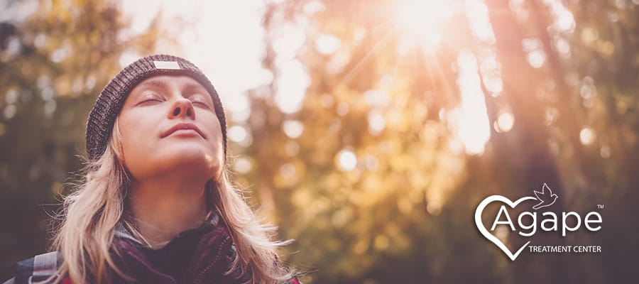 Person wearing a beanie and closed eyes in sunlight with Agape Treatment Center logo.