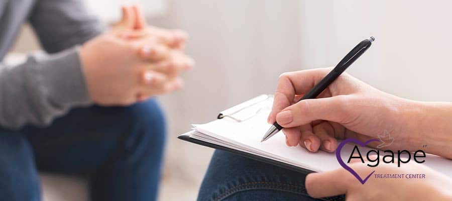 Person holding pen and clipboard, logo of Agape Treatment Center visible.