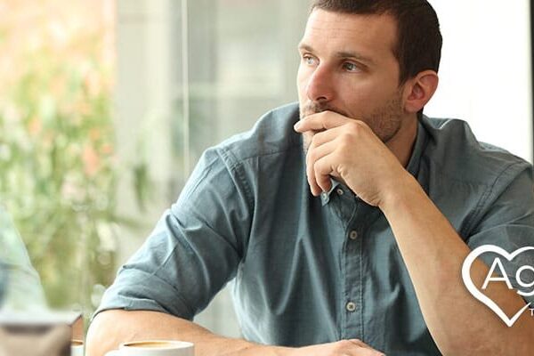 Person in a blue shirt sitting at a table, looking thoughtful.