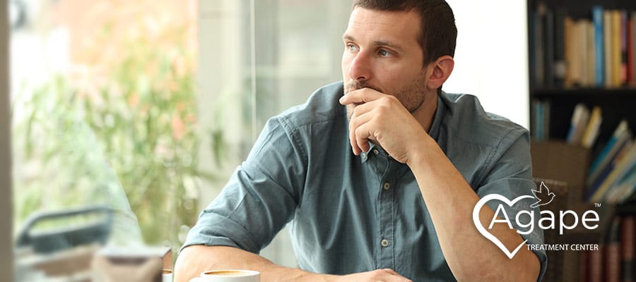 Person in a blue shirt sitting at a table, looking thoughtful.