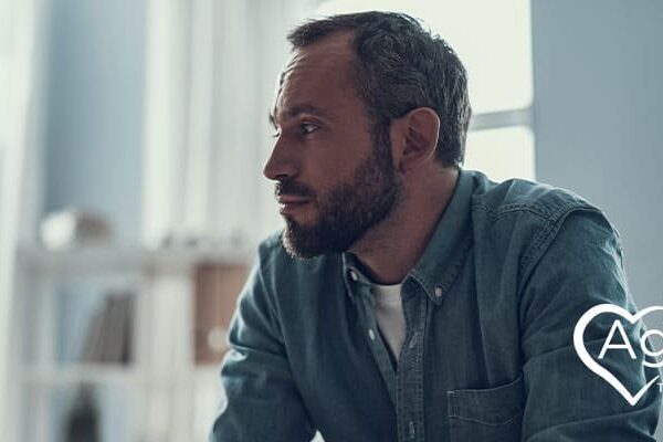 Person in denim shirt sitting and looking thoughtful with Agape Treatment Center logo.