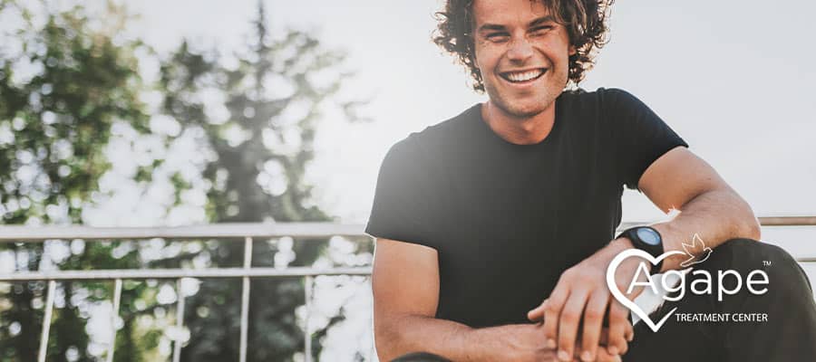 Person in black shirt smiling, Agape Treatment Center logo.