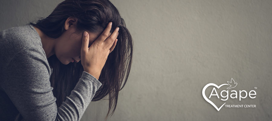 Person in gray shirt sitting with hands on head.