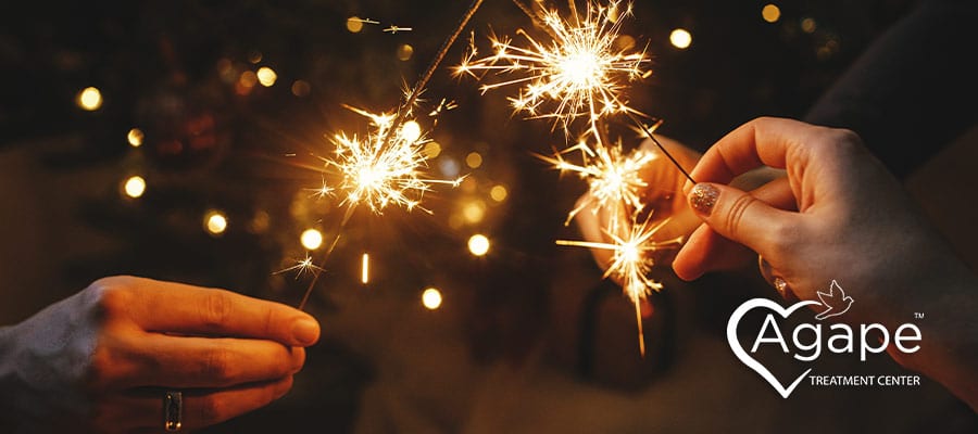 People holding sparklers with Agape Treatment Center logo visible.