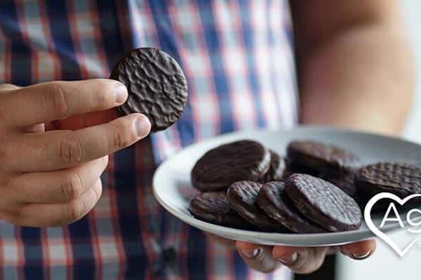 Person in checkered shirt holding plate of chocolate cookies.