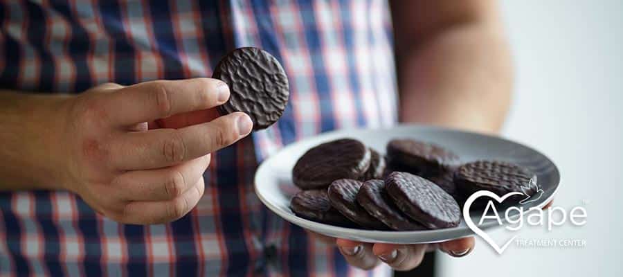 Person in checkered shirt holding plate of chocolate cookies.